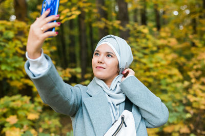 Portrait of young woman photographing through smart phone