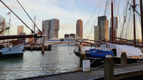 Sailboats moored in harbor by city against sky