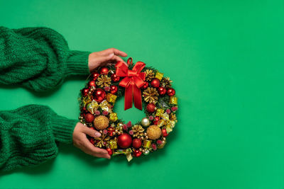 Christmas fir wreath with festive decor in female hands on green background