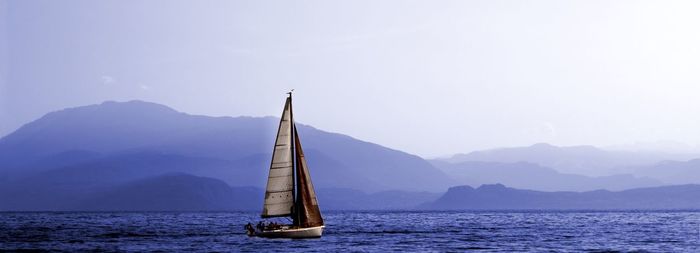 Sailboat sailing on sea against mountains