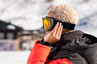A african american woman wearing goggles standing in snowy mountain during winter	