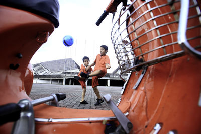 Boys playing with ball seen through red motor scooter