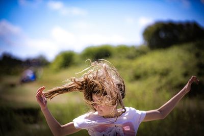 Girl with arms raised on field against sky