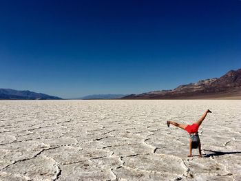 Woman with umbrella on desert against clear blue sky