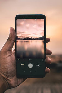 Close-up of hand holding smart phone against sky during sunset