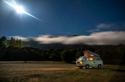 Car on illuminated field against sky at night