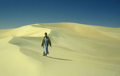 Rear view of woman walking on sand dune in desert against clear sky