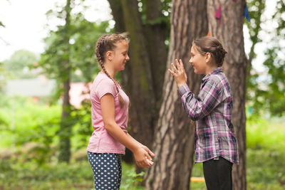 Side view of siblings standing against trees