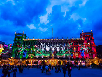 Crowd on illuminated city against blue sky