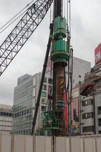 Low angle view of crane amidst buildings against sky