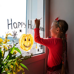 Child painting pumpkin window preparing celebrate halloween kid draws decorates room with paper bats