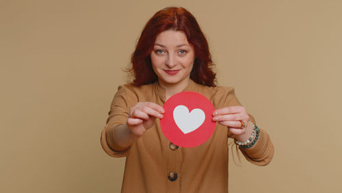 Portrait of young woman holding heart shape against pink background