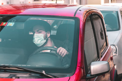 Young man wearing mask driving car in traffic