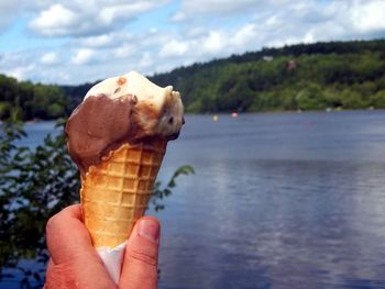 Cropped hand of person holding ice cream cone against lake