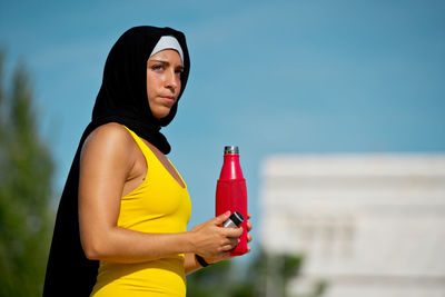 Side view of woman in hijab holding bottle outdoors