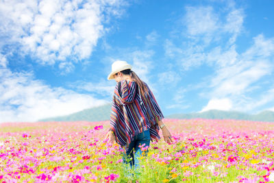 Woman standing by pink flowering plants on field against sky