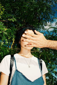 Cropped hand of man covering woman face against trees