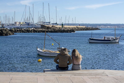 Rear view of two people sitting in harbor