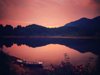 Scenic view of lake by silhouette trees against orange sky