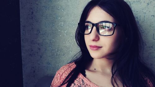 Close-up of young woman wearing eyeglasses against wall