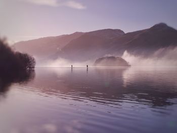 Scenic view of lake and mountains against sky. paddle boarders on misty lake. morning mist.