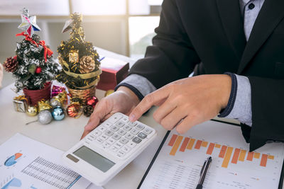 Midsection of businesswoman writing on graph while colleague using calculator with christmas decorations on table