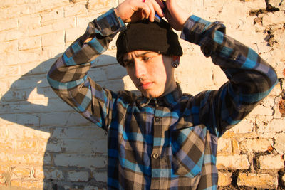 Young man wearing knit hat standing by wall outdoors