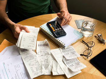 Man is making audit of household expenses using calculator and notebook. lots of receipts and bills