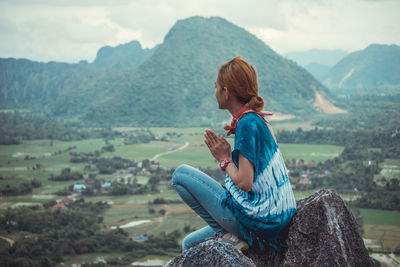 Side view of mid adult woman sitting on cliff against mountains
