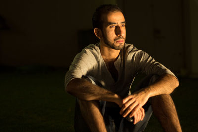 Man looking away while sitting on field at night