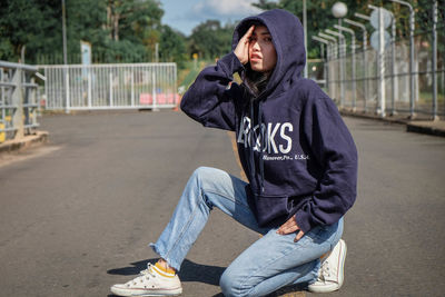 Portrait of young woman wearing hooded shirt while crouching on street