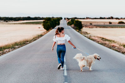 Rear view full length of woman walking with dog on road