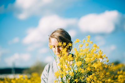 Close-up of woman by yellow flower on field against sky