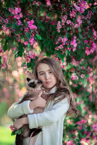 Portrait of girl with cat standing against flowering plant