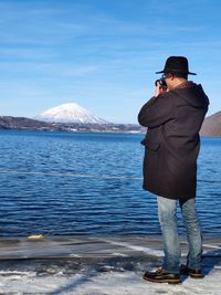 Man photographing lake and snowcapped mountain against sky