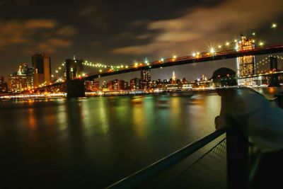 Illuminated bridge over river against sky in city at night