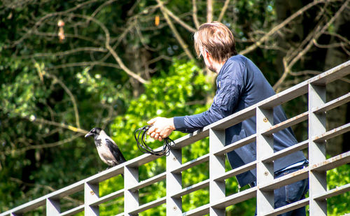 Rear view of man leaning on railing against trees