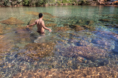 Young man wearing sun glass sitting on rock in flowing river clear water at morning from flat angle