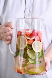 A jug with organic soft drink with ripe fresh strawberries, lemon slices with lime and basil, 