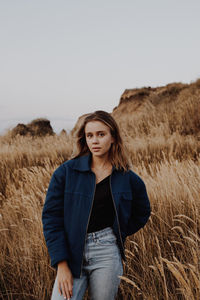 Portrait of young woman standing on field against sky