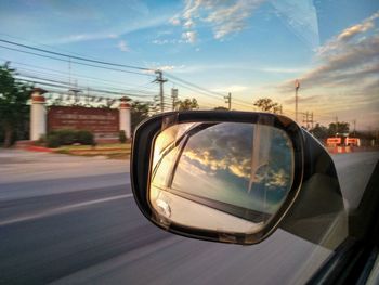 Close-up of side-view mirror against sky