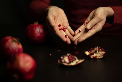 Women's elegant white hands red pomegranate seeds hands table symbolize feminine nature