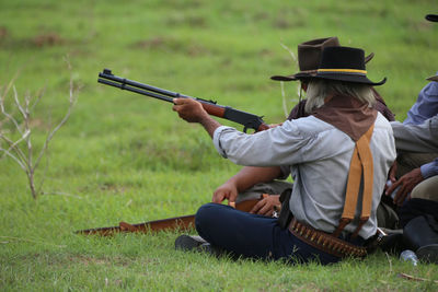 Rear view of men with rifle sitting on grassy field