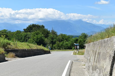 Empty road along trees and mountains against sky