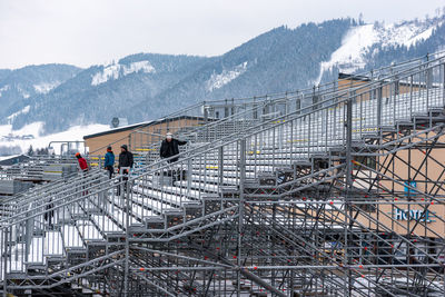 People on footbridge against mountains during winter