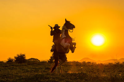 Silhouette cowboy riding a horse carrying a gun under beautiful sunset