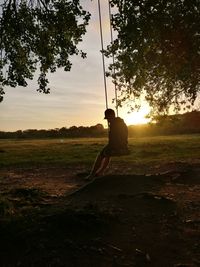 Silhouette man on tree against sky during sunset