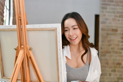 Young woman by canvas against brick wall