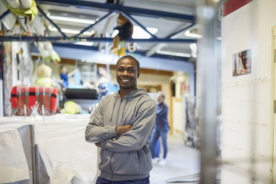 Portrait of smiling mid adult male volunteer standing with arms crossed in warehouse