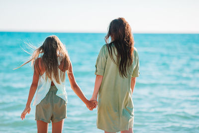 Rear view of girls holding hand standing on beach